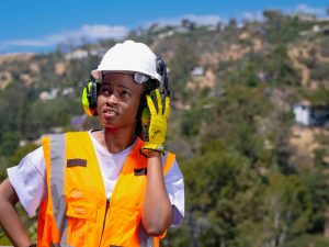 Female construction worker wearing PPE equipment including hardhat and reflective vest, in an outdoor setting.